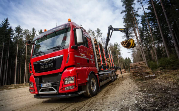 4K Ultra HD image of a red logging truck with a man operating a crane in a forest setting, designed as a PC desktop wallpaper and background.