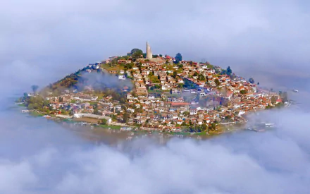 A serene view of Lake Patzcuaro in Mexico, shrouded in fog with a man-made island town nestled on a hill, showcasing its unique charm and beauty.