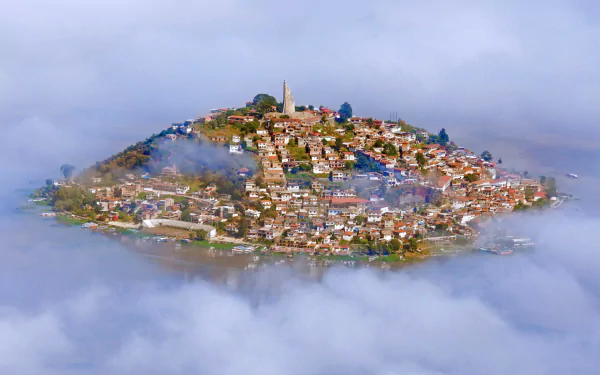 A serene view of Lake Patzcuaro in Mexico, shrouded in fog with a man-made island town nestled on a hill, showcasing its unique charm and beauty.