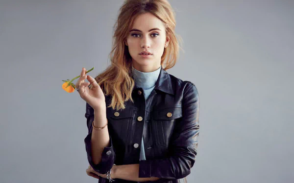 HD desktop wallpaper of a brunette model with brown eyes holding a small orange flower, posed against a neutral gray backdrop.