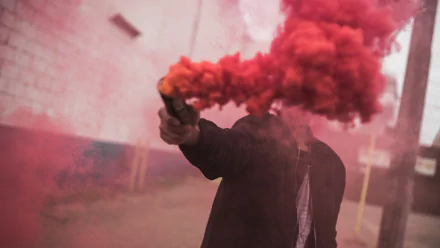 HD desktop wallpaper featuring a person holding a red smoke flare, creating vibrant red smoke against an urban backdrop in this striking photography shot.