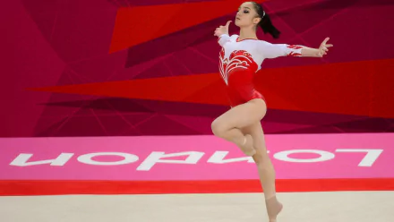 Gymnast mid-leap in a red-and-white leotard on a pink competition mat, dynamic sports action — HD PC desktop wallpaper/background.