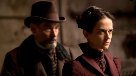A dramatic scene from the TV show Penny Dreadful, featuring a stern woman in Victorian attire with a serious expression, as a man in a hat looms closely behind her.