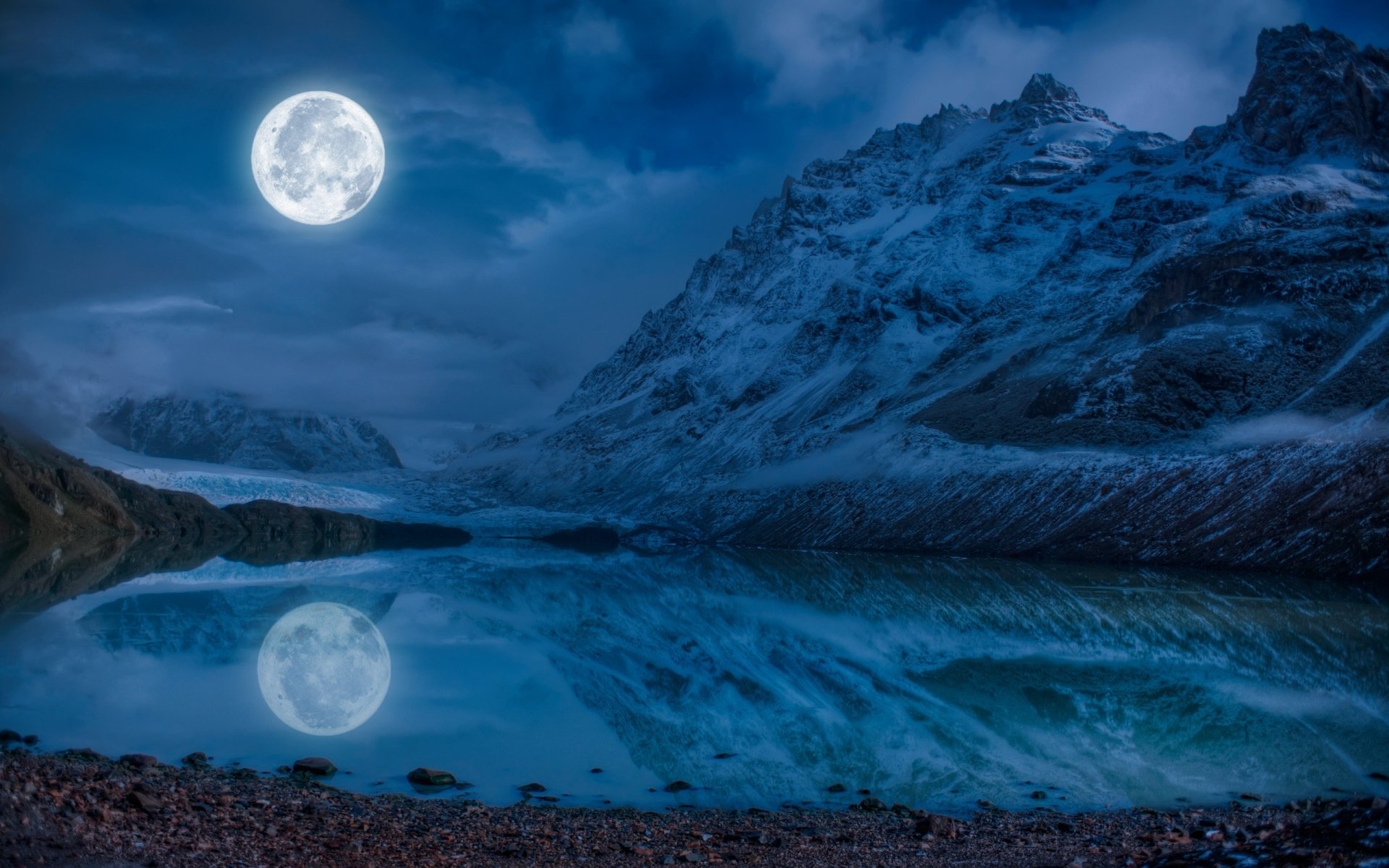 A serene winter landscape featuring a snow-covered mountain reflecting in a calm blue lake, illuminated by a glowing full moon. Captivating nature scene for a HD wallpaper.