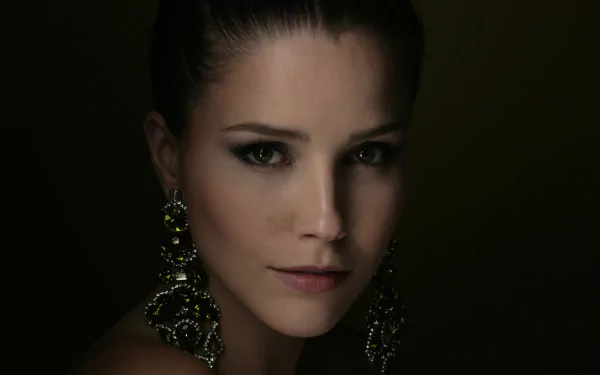 Close-up HD portrait of brunette American actress Sophia Bush with striking earrings against a dark background, capturing her face in soft, dramatic lighting.