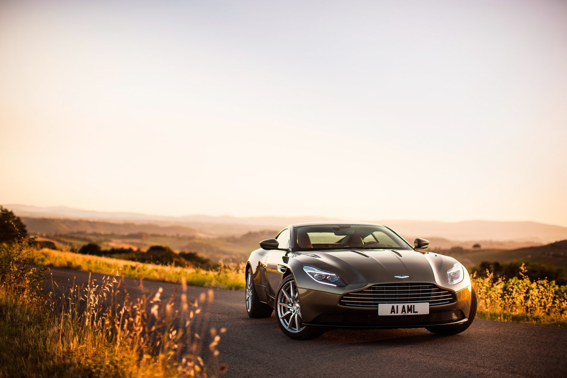 A sleek Aston Martin DB11 grand tourer parked on a scenic road at sunset, captured in 4K Ultra HD for a stunning PC desktop wallpaper.