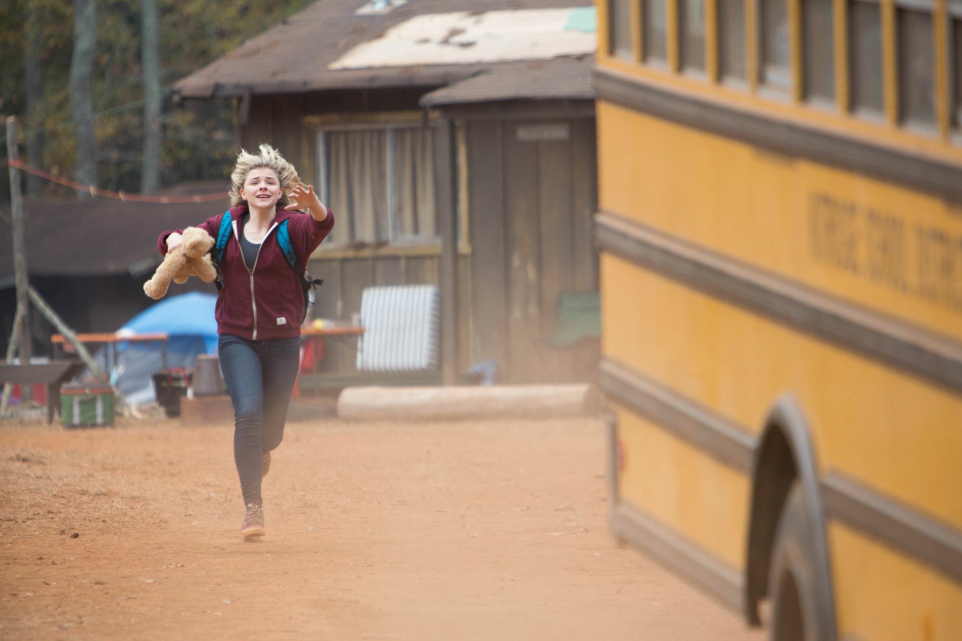 Chloë Grace Moretz running with a teddy bear near a yellow school bus in a scene from the movie The 5th Wave, rendered as a 4K Ultra HD PC desktop wallpaper.