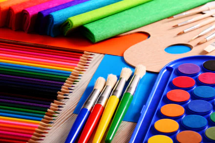 A vibrant assortment of art supplies, including colorful pencils, brushes, and paints, arranged on a wooden surface, showcased in a 4K Ultra HD desktop wallpaper.