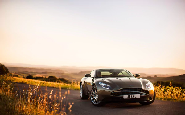 A sleek Aston Martin DB11 grand tourer parked on a scenic road at sunset, captured in 4K Ultra HD for a stunning PC desktop wallpaper.