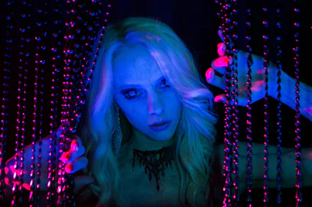 Blonde woman amid hanging beads, bathed in neon blue and magenta light — 5K Ultra HD PC desktop wallpaper depicting a scene from the movie Scouts Guide to the Zombie Apocalypse