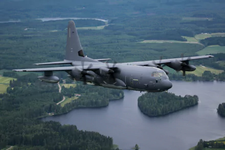 Lockheed C-130 Hercules military transport aircraft flies over a forested landscape with rivers, captured in HD for a striking warplane desktop wallpaper.