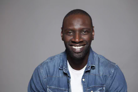 Smiling French actor Omar Sy against a neutral gray background in a 4K Ultra HD desktop wallpaper.