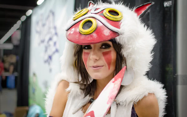Woman with brown hair wearing a Princess Mononoke cosplay mask and necklace, smiling confidently in a 4K Ultra HD PC desktop wallpaper by Jessica Nigri.