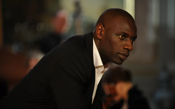 Cinematic close-up of a man in a black suit leaning forward in a dimly lit room; 4K Ultra HD PC desktop wallpaper background.