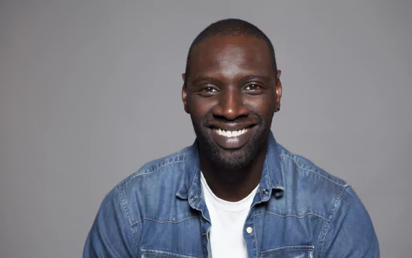 Smiling French actor Omar Sy against a neutral gray background in a 4K Ultra HD desktop wallpaper.