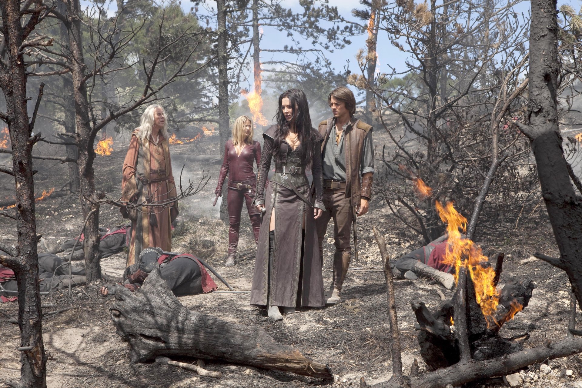 Legend of the Seeker TV scene: four figures stand in a scorched forest among burning debris; 5K Ultra HD PC desktop wallpaper background.