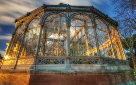 Close-up HD desktop wallpaper of a man-made glass gazebo illuminated at dusk, showcasing intricate metal framework and surrounding trees under a dramatic sky.