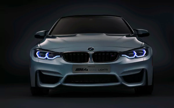 Front view of a silver BMW M4 Coupe grand tourer with illuminated blue headlights against a dark background, shown in 4K Ultra HD quality.