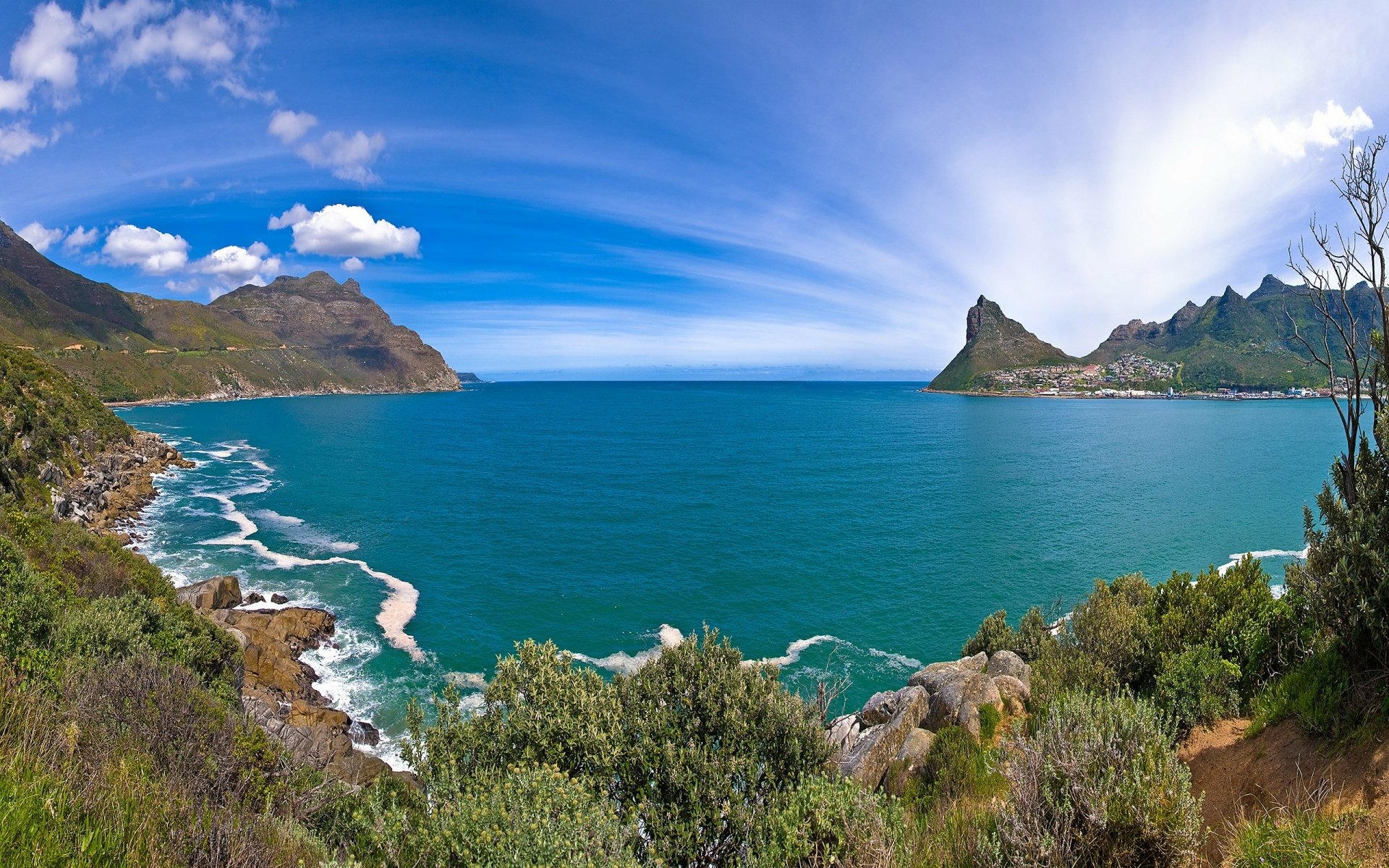 HD desktop wallpaper showcasing a vibrant coastline with lush bushes, calm ocean waters, and a clear blue horizon under a partly cloudy sky.