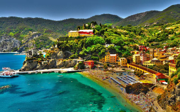 HD desktop wallpaper of Monterosso al Mare, a colorful Italian town along the coastline with vibrant buildings overlooking the clear blue ocean and lush green hills.
