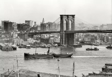 Black and white HD desktop wallpaper of the Brooklyn Bridge spanning the river with boats and city buildings in New York, USA.