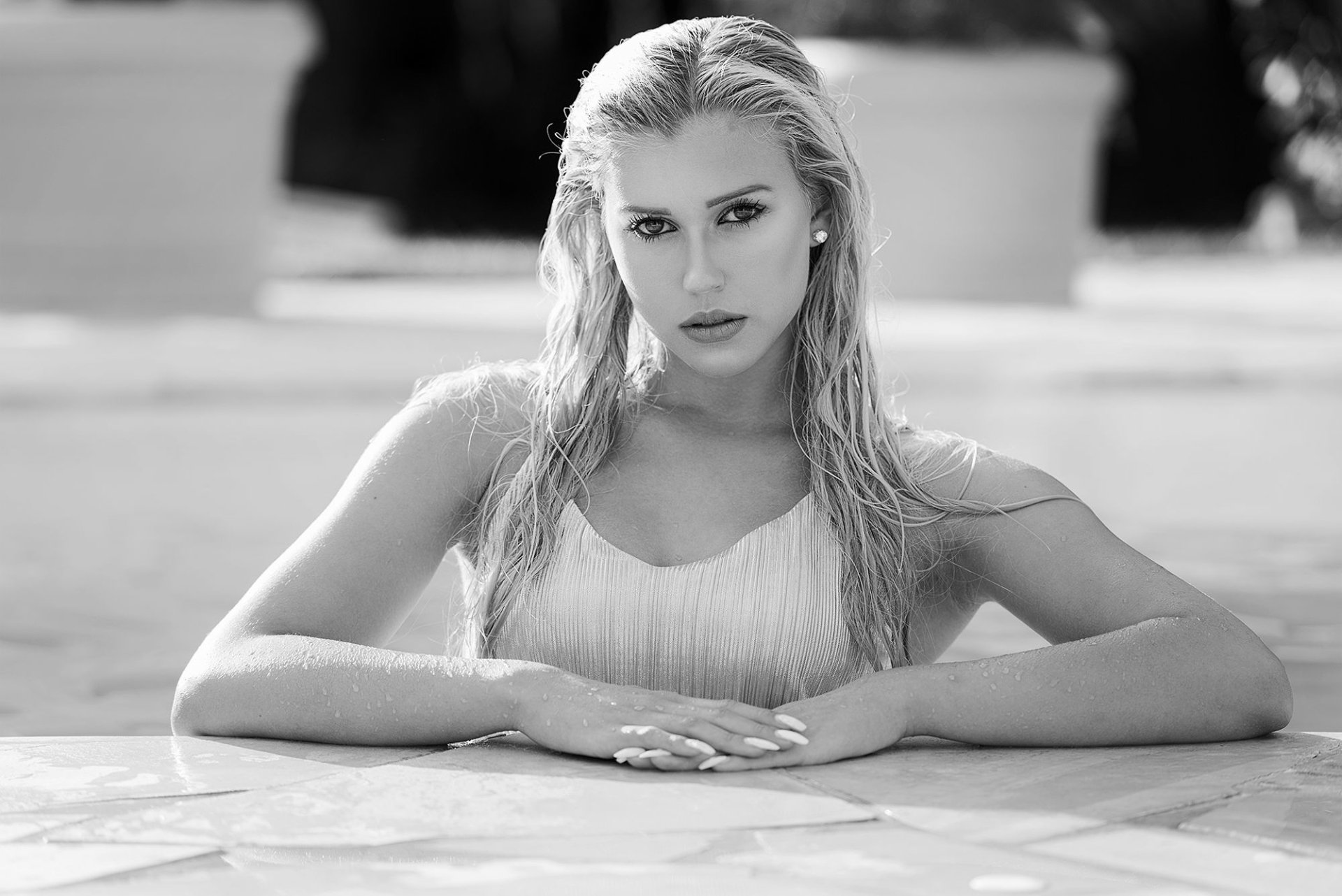 Black and white HD desktop wallpaper featuring a woman model with wet hair, leaning on the edge of a pool, gazing directly at the camera.