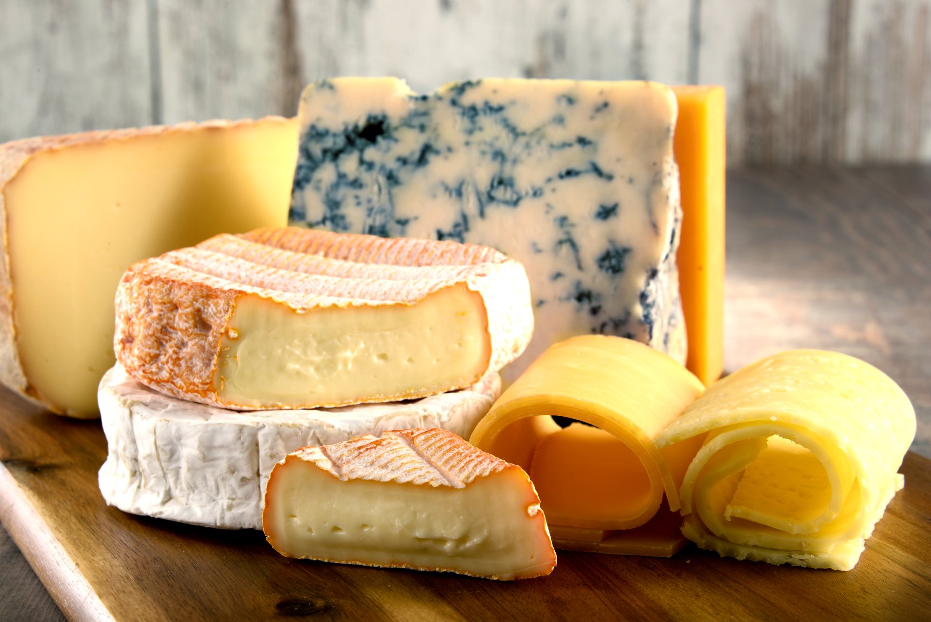 A vibrant collection of assorted cheeses, including brie, blue cheese, and cheddar, arranged on a wooden board, designed as a 4K Ultra HD PC desktop wallpaper and background.