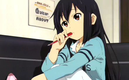 Azusa Nakano from the anime K-ON! is shown in a detailed HD desktop wallpaper, thoughtfully holding a pencil while seated indoors.