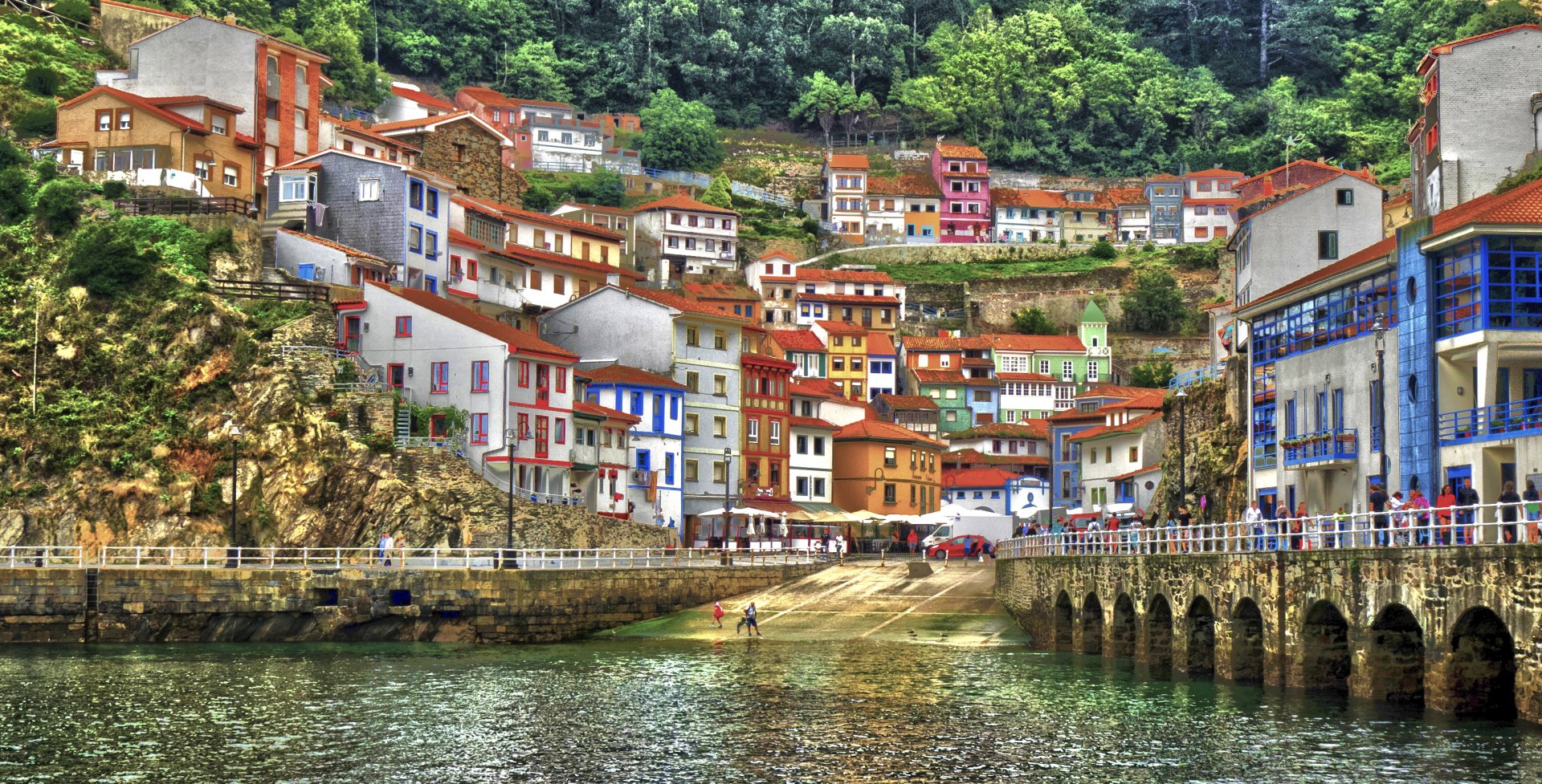 2K Quad HD PC wallpaper of Cudillero, Spain — colorful hillside houses clustered above an arched stone bridge and tranquil harbor in a seaside village.