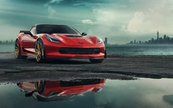 A red Chevrolet Corvette (C7) parked on wet ground with its sharp reflection visible, under a cloudy sky with a distant city skyline in the background.