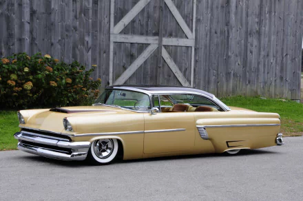 Gold 1956 Mercury (vehicle) lowrider hot rod with slammed stance parked by a wooden barn — HD PC desktop wallpaper background.