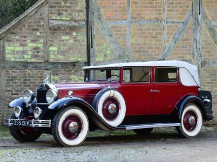 HD PC desktop wallpaper showing a crimson 1931 Packard Standard Eight Convertible Sedan vintage car parked before a brick-and-timber wall, with whitewall tires and folded soft top.