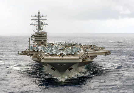 HD desktop wallpaper of the USS Ronald Reagan (CVN-76) aircraft carrier at sea, showcasing its military warship design and deck loaded with aircraft.