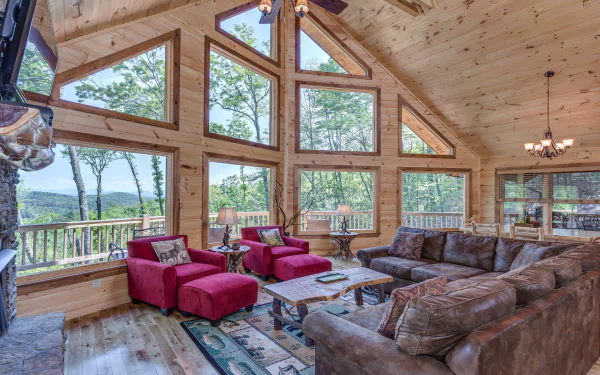 HD PC desktop wallpaper of a mountain cabin lodge interior — a man-made, wood-paneled room with large windows, plush seating and sweeping forested mountain views.