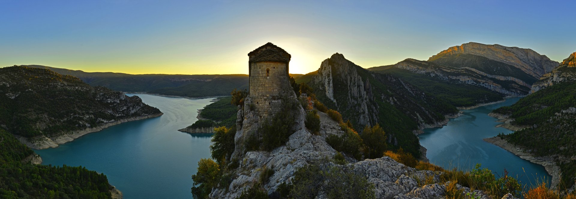A stunning landscape of a fortress overlooking the Mare de Déu de la Pertusa lake in Spain, captured at sunrise, showcasing the natural beauty of the region.