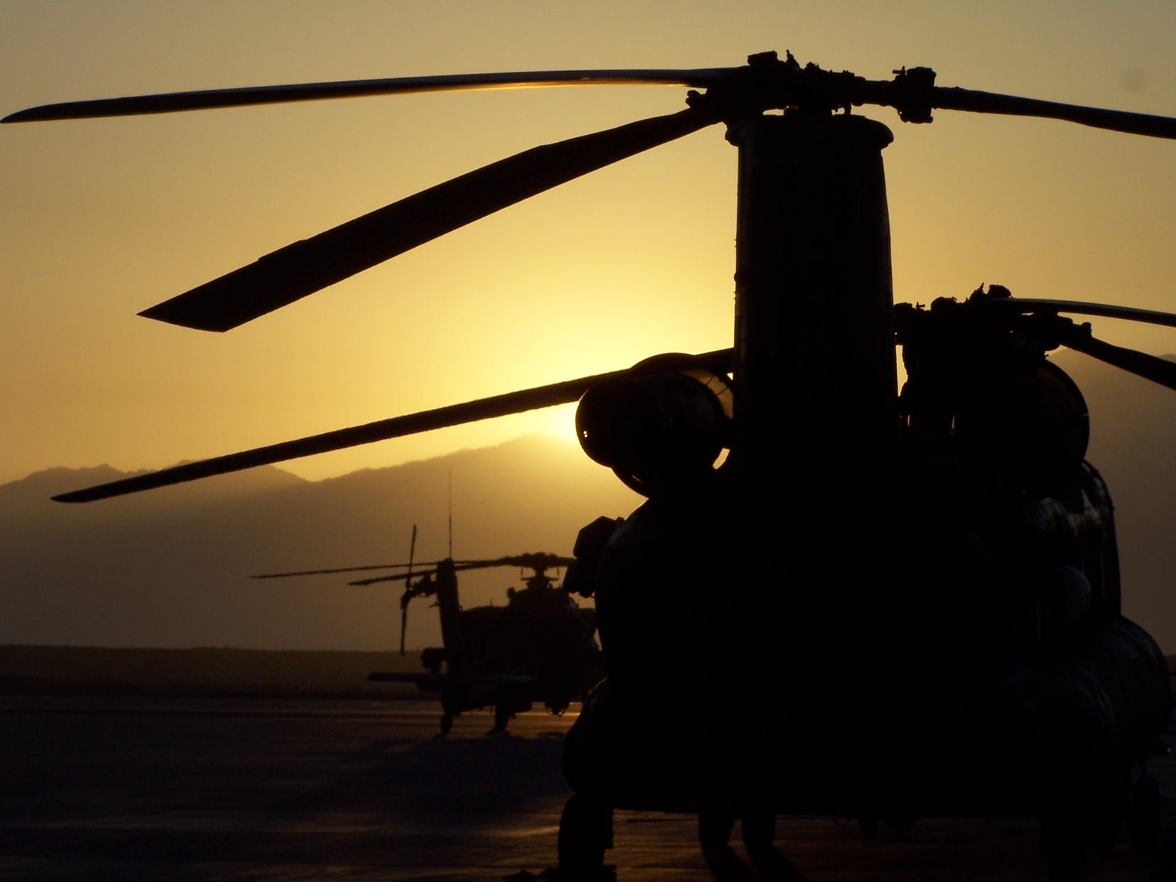 A stunning HD desktop wallpaper featuring military helicopters silhouetted against a glowing sunset, showcasing their powerful rotors and dynamic presence.