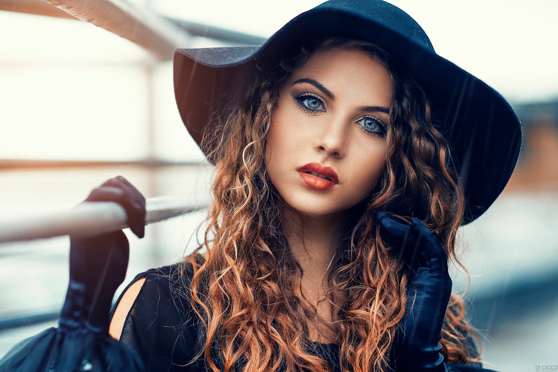 HD desktop wallpaper featuring a brunette model with blue eyes, wearing a hat and black gloves, leaning on a railing.