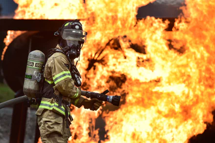 A firefighter in full gear uses a hose to control intense flames in this HD desktop wallpaper background.