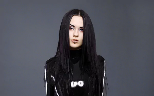 A brunette woman models a sleek latex outfit, showcasing her striking look and piercing features against a minimalist gray background. High-definition desktop wallpaper.