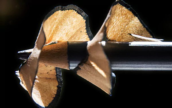 4K Ultra HD photography of a sharpened black pencil with curled wood shavings against a dark backdrop — PC desktop wallpaper/background.