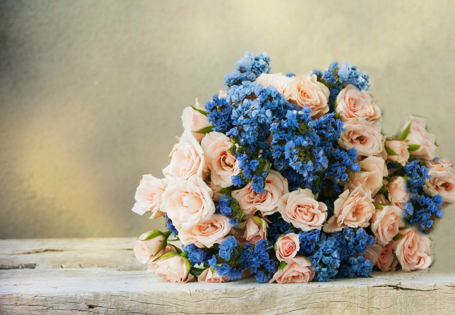 HD PC desktop wallpaper showing a man-made bouquet of peach roses and vivid blue flowers resting on a weathered white table.
