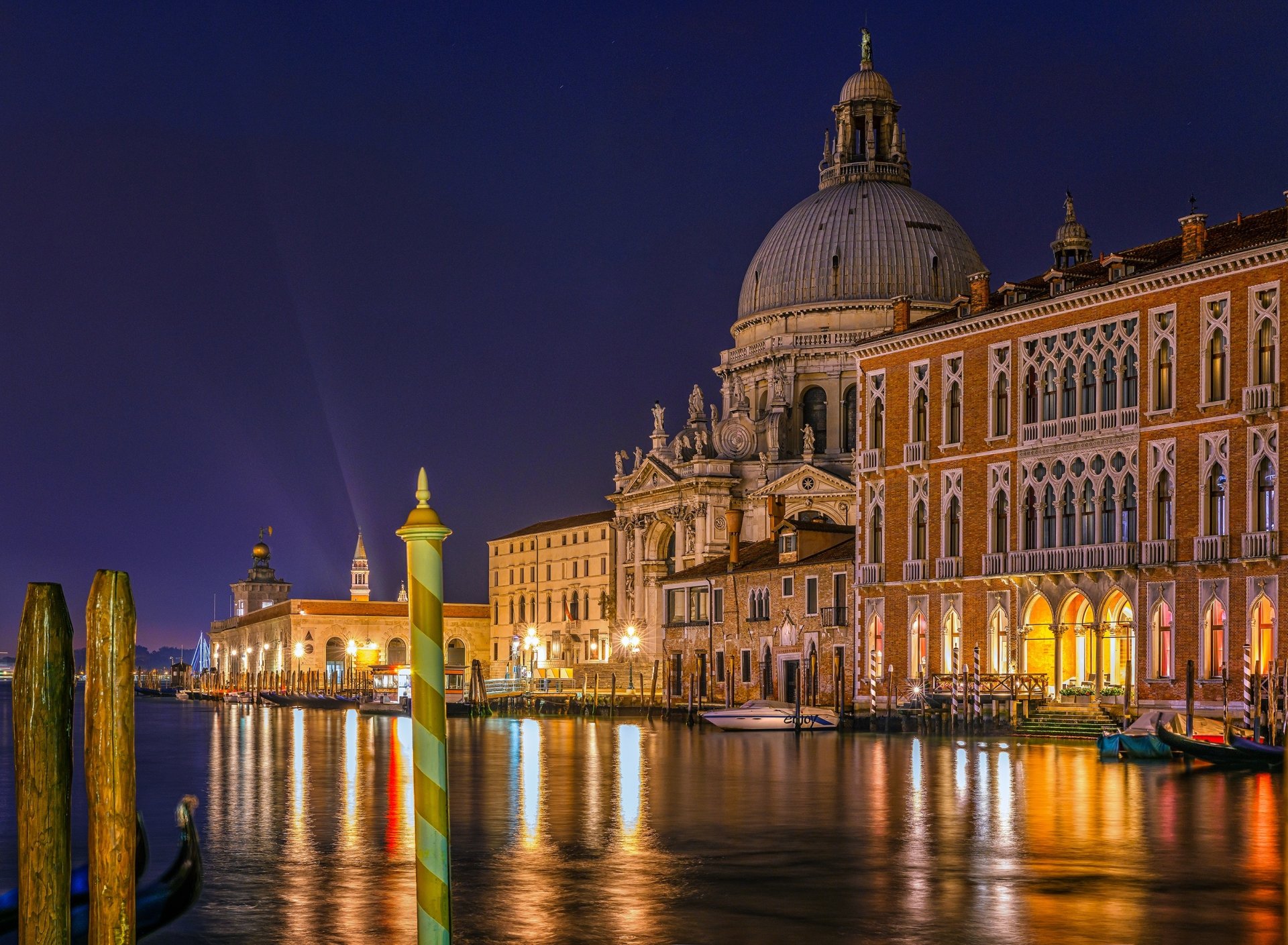 Night view of Venice's Grand Canal featuring illuminated historic architecture and a prominent dome, reflecting beautifully on the water.