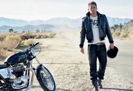 2K Quad HD PC wallpaper: American actor in a leather jacket walking along a desert road beside a Triumph motorcycle, holding a helmet.