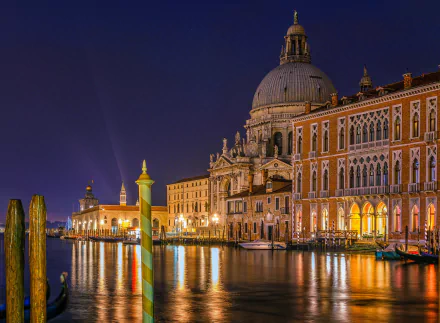Night view of Venice's Grand Canal featuring illuminated historic architecture and a prominent dome, reflecting beautifully on the water.