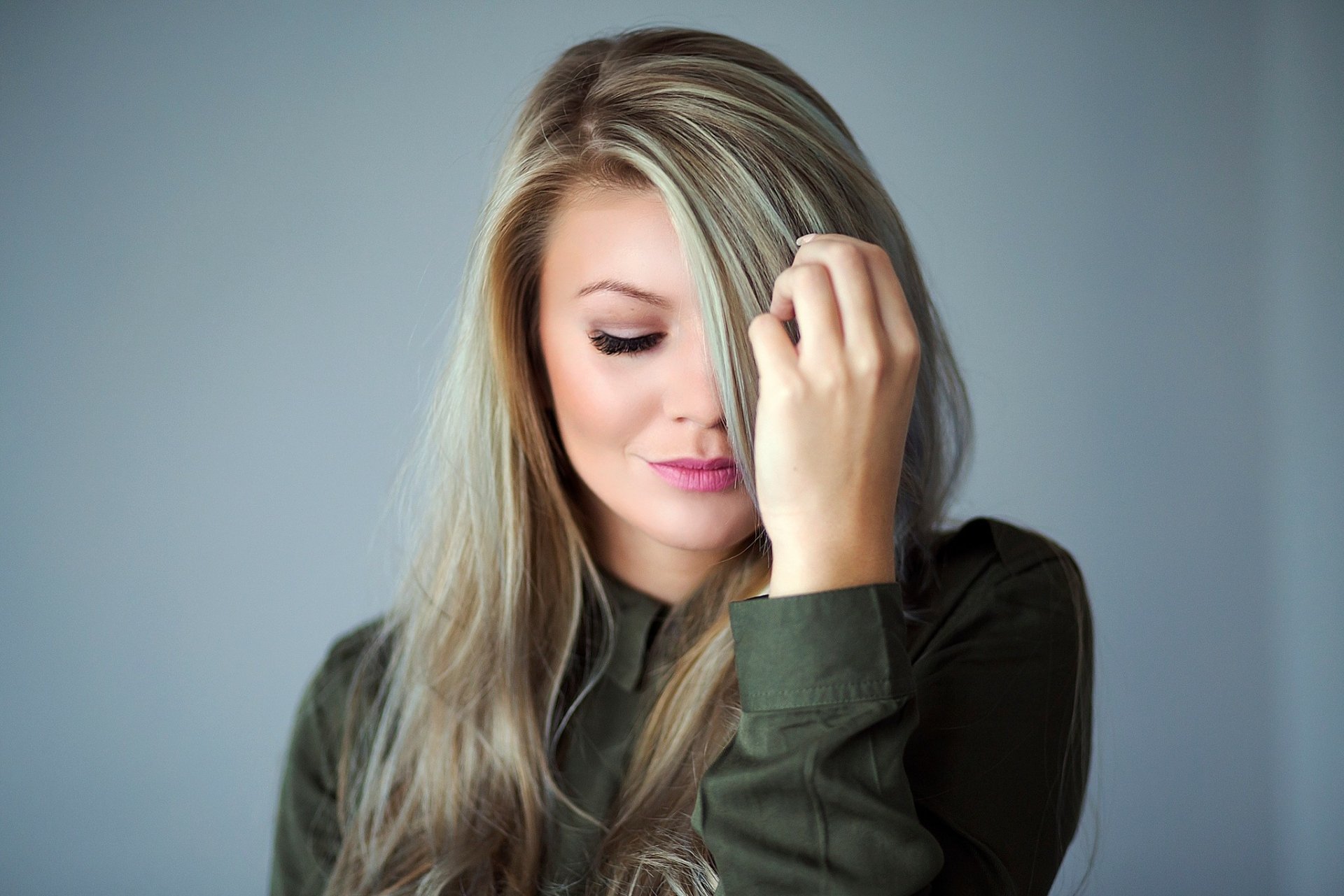 A close-up of a blonde woman with long hair, gently touching her face, against a soft background. This high-definition image serves as a stylish desktop wallpaper.