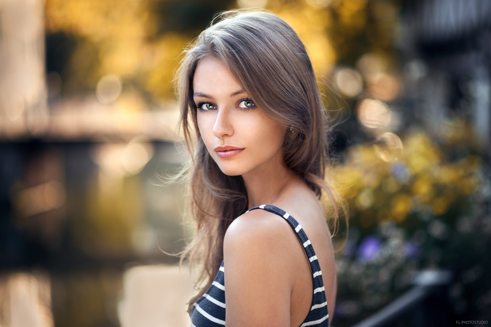 HD desktop wallpaper of a brunette woman model with striking blue eyes, set against a softly blurred bokeh background.