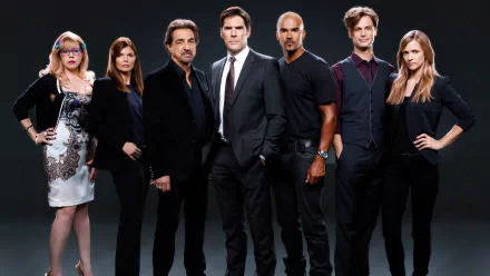 A group portrait of the main cast from the TV show *Criminal Minds*, featuring diverse characters in formal and casual attire, set against a dark background.