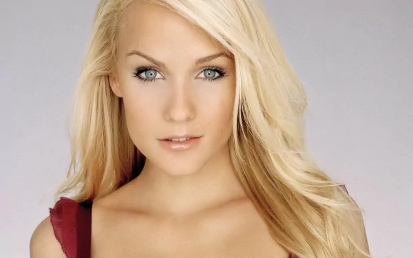 A high-definition desktop wallpaper featuring Mirjam Weichselbraun, a woman with long blonde hair and striking blue eyes, gazing directly at the camera with a neutral expression against a light background.