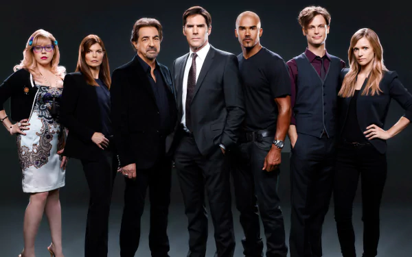 A group portrait of the main cast from the TV show *Criminal Minds*, featuring diverse characters in formal and casual attire, set against a dark background.