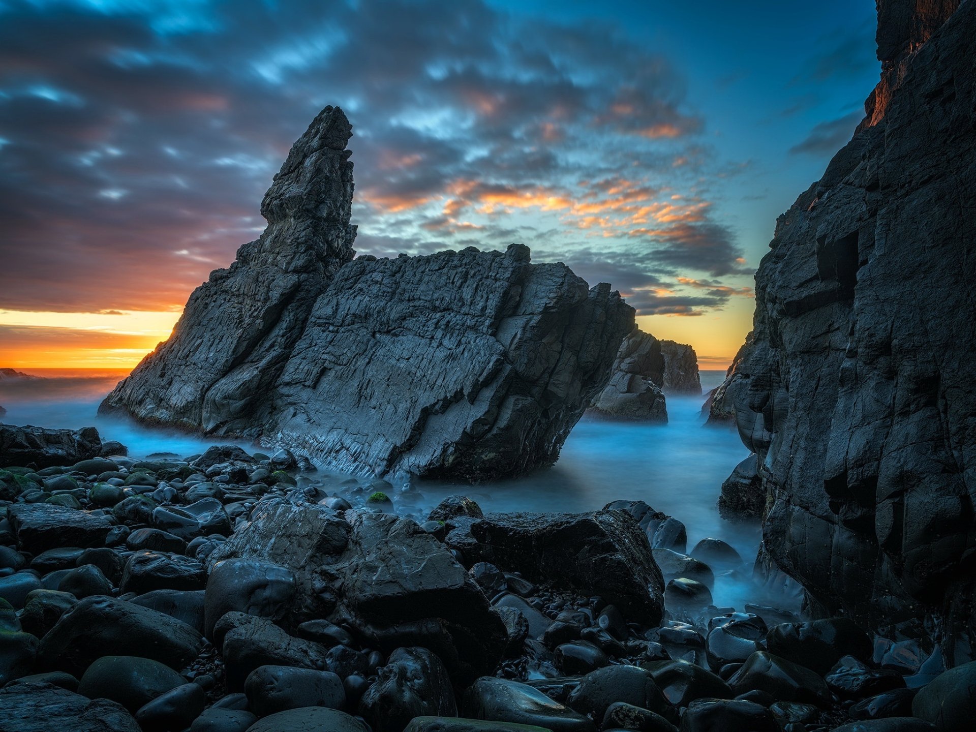 HD PC desktop wallpaper/background of a dramatic sunset over a rocky coast — jagged rock formations and calm surf beneath a colorful sky, a tranquil nature scene.